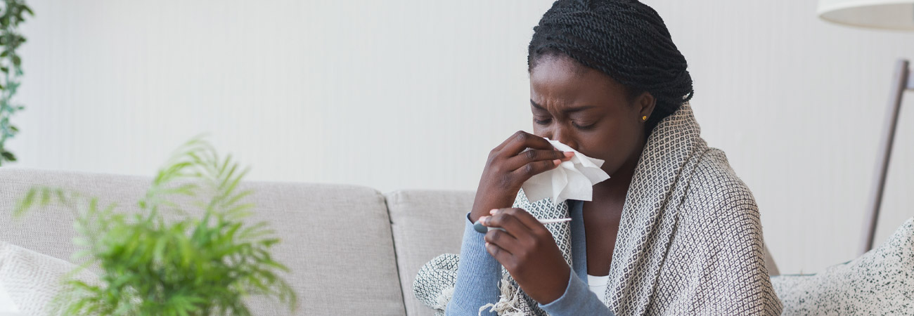 Woman sitting on couch sneezing into tissue