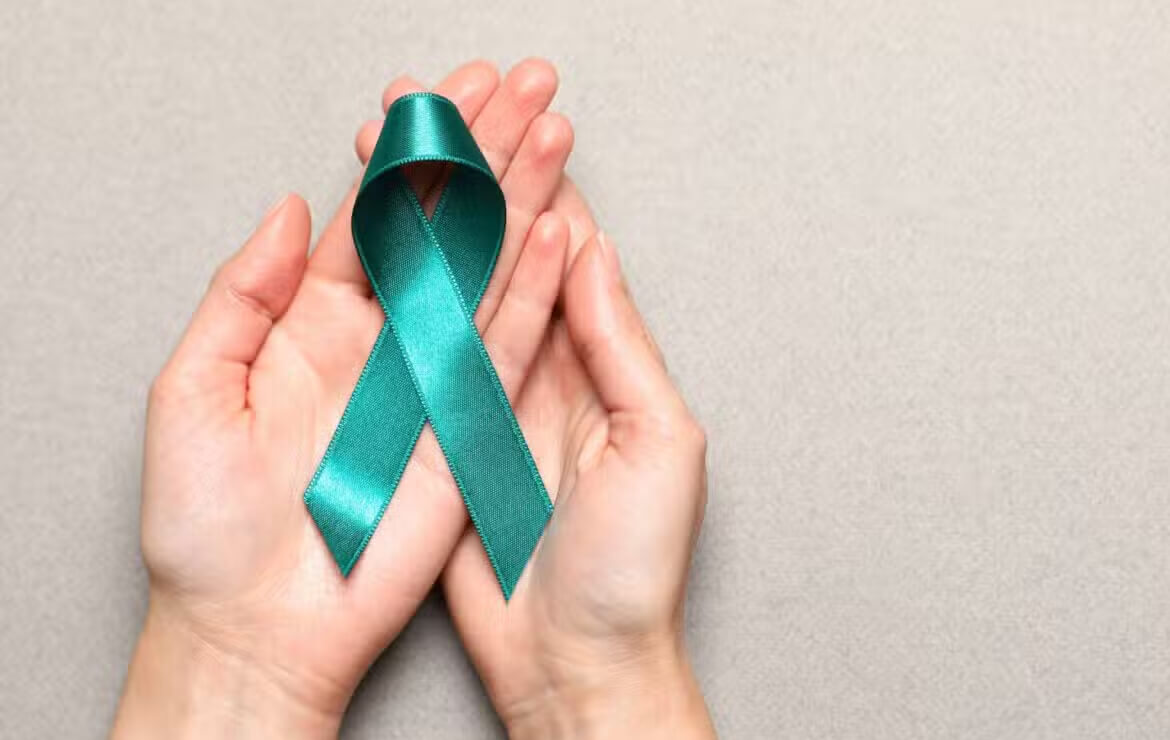 Hand holding teal green ribbon for cervical cancer awareness month