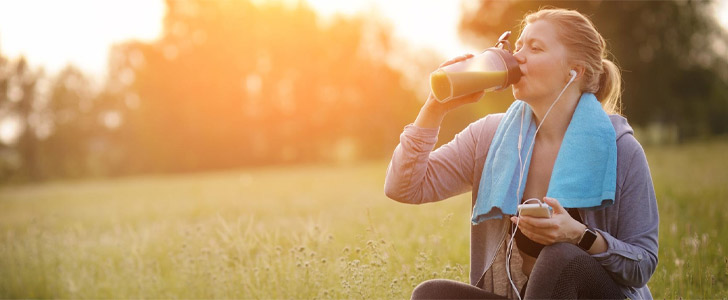 Woman sitting outside drinking protein shake after workout