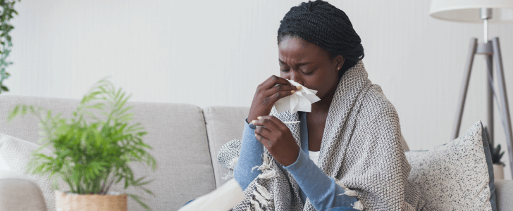 Woman sitting on sofa sneezing into tissue