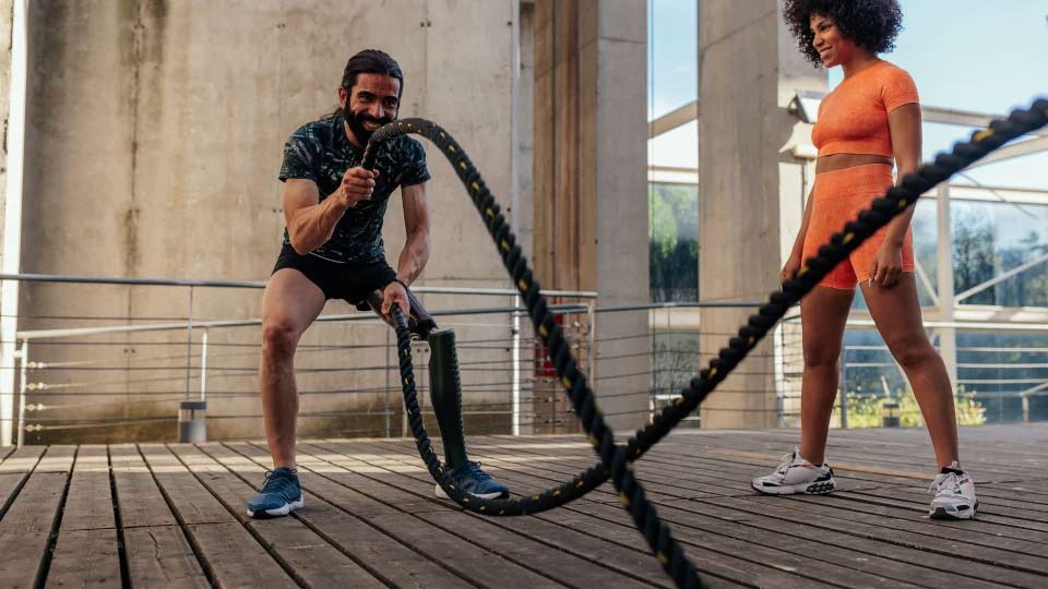 Man and woman outside exercising arms with ropes