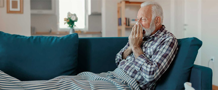 Older man sitting on couch sneezing into tissue