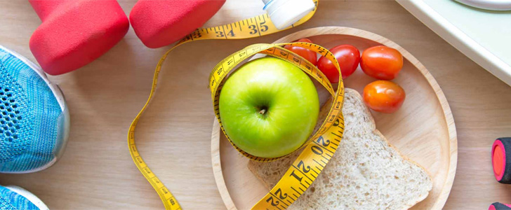 Hand weights, running shoes, measuring tape and green apple