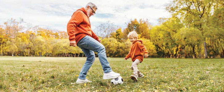 Grandfather and grandson playing soccer together in large park